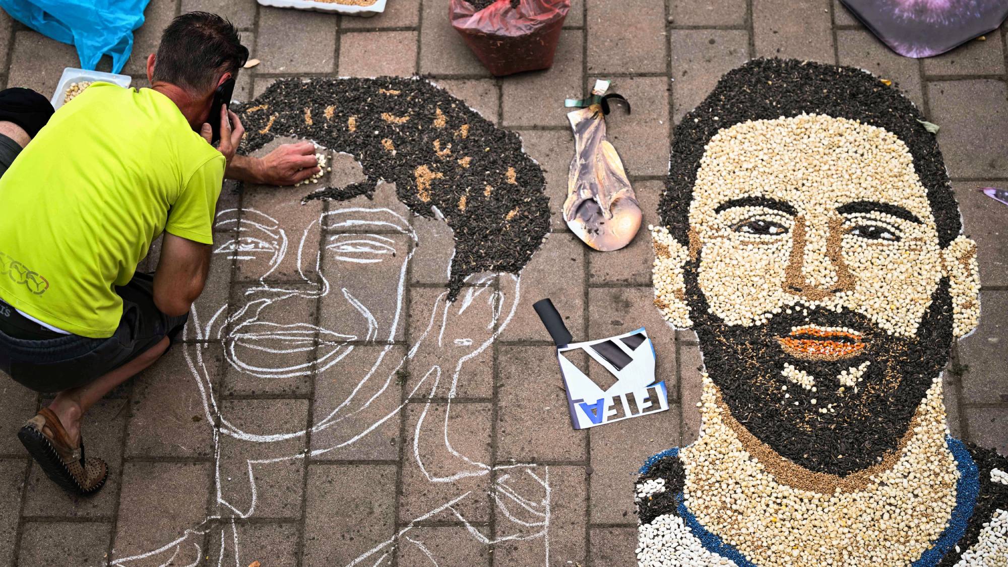 Kosovar artist Alkent Pozhegu works on a mosaic on the ground, made with grain and seeds, and depicting Argentina's forward #10 Lionel Messi (R) and Spain's forward #19 Lamine Yamal, in the town of Gjakova on July 16, 2026. Thousands of kilometres away from New York, where the Argentina and Spain football teams will compete for the World Cup title, in the western city of Gjakova, Alkent Pozhegu has made a mosaic depicting the two forward stars Lionel Messi and Lamine Yamal.